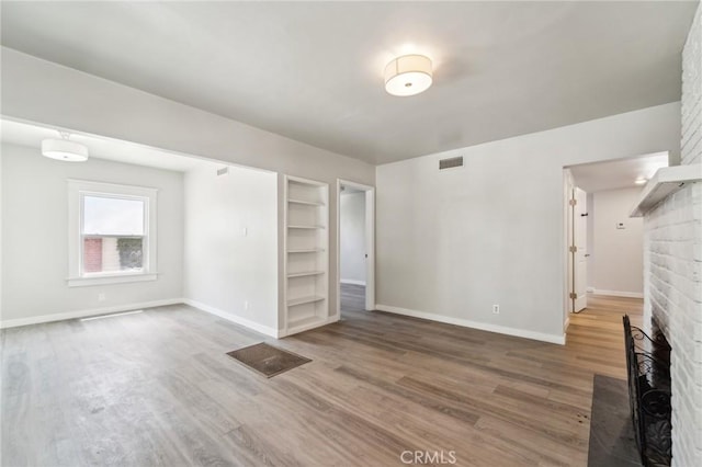 unfurnished living room featuring wood finished floors, built in shelves, baseboards, and a fireplace