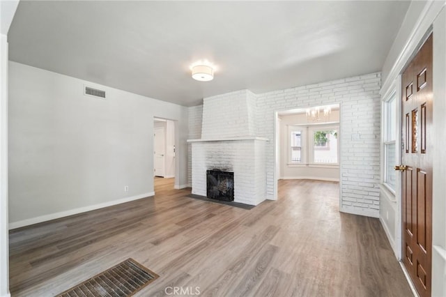 unfurnished living room with wood finished floors, a brick fireplace, baseboards, and a chandelier