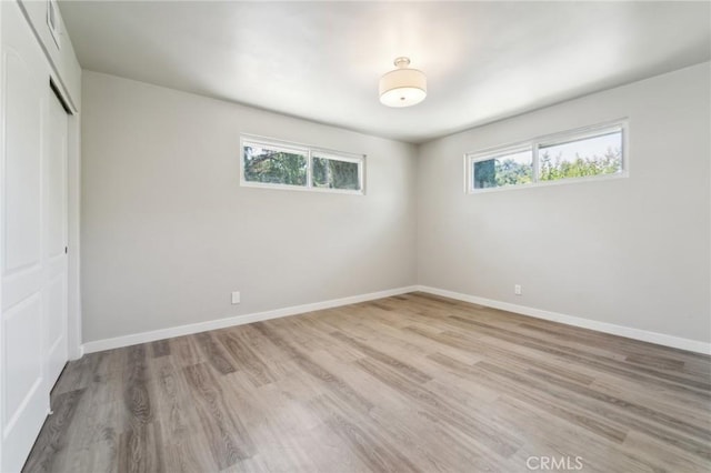 unfurnished bedroom with multiple windows, a closet, light wood finished floors, and baseboards