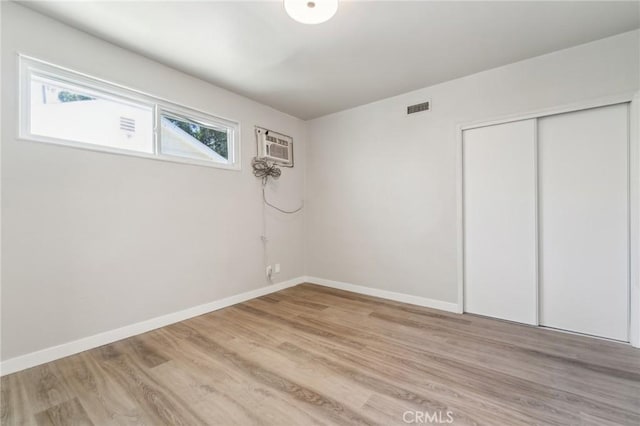 unfurnished bedroom featuring light wood finished floors, a closet, a wall mounted AC, and baseboards