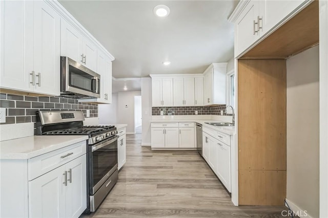 kitchen with appliances with stainless steel finishes, a sink, recessed lighting, backsplash, and light wood-type flooring