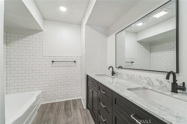 bathroom featuring wood finished floors, double vanity, a tub to relax in, and tile walls