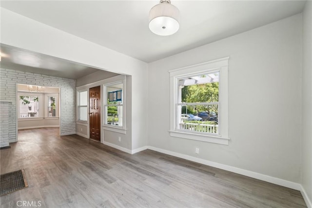 unfurnished room with wood finished floors, baseboards, and brick wall