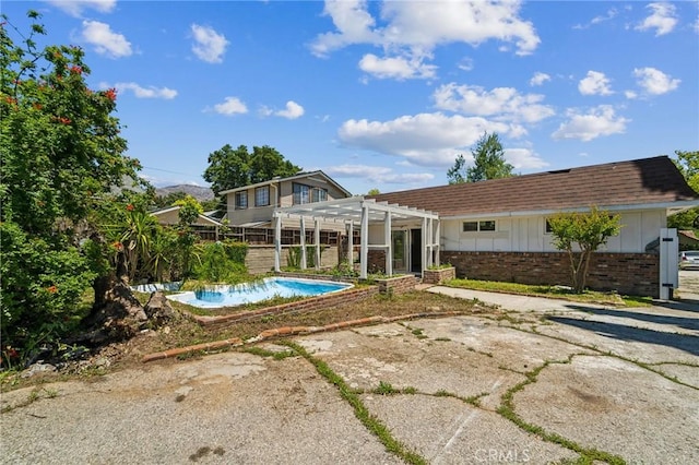 rear view of house featuring a pergola, an outdoor pool, brick siding, and board and batten siding