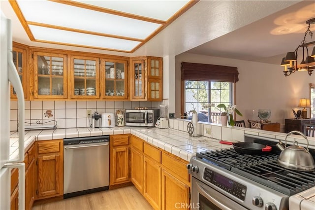919 S Waldstrasse Way, Big Bear Lake, CA 92314 - kitchen featuring appliances with stainless steel finishes, backsplash, a chandelier, light wood-type flooring, and glass insert cabinets