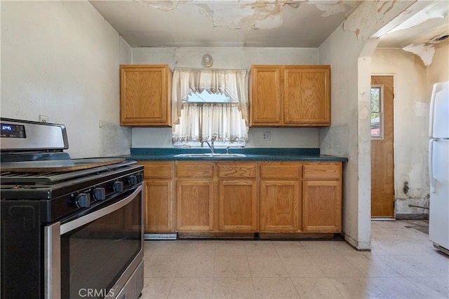 kitchen with stainless steel gas range, a sink, dark countertops, freestanding refrigerator, and brown cabinetry