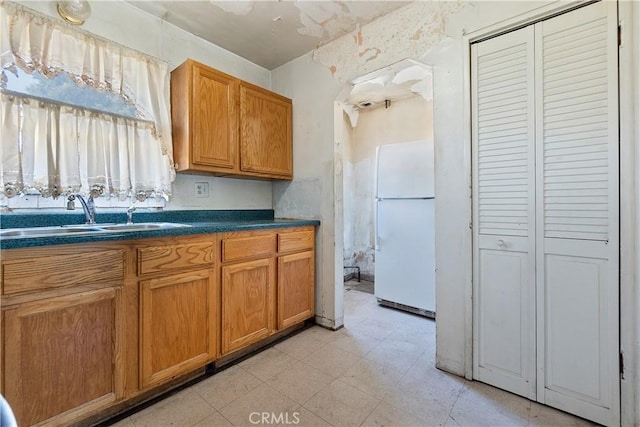 kitchen with freestanding refrigerator, a sink, dark countertops, and brown cabinetry