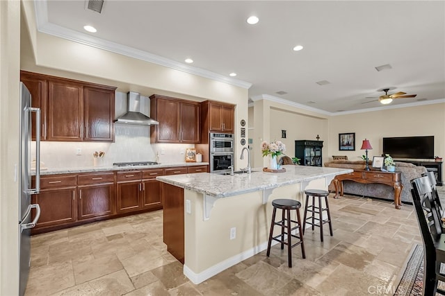 kitchen with wall chimney exhaust hood, appliances with stainless steel finishes, stone tile floors, crown molding, and a breakfast bar area