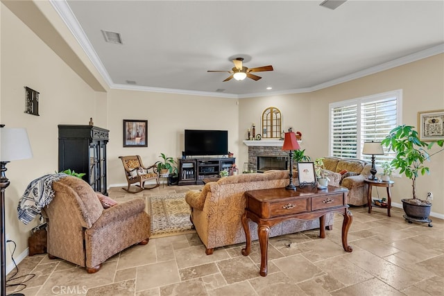 living room featuring a ceiling fan, baseboards, a stone fireplace, crown molding, and stone tile flooring