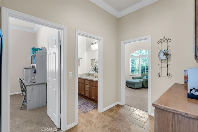 hallway featuring ornamental molding, stone tile floors, baseboards, and a sink