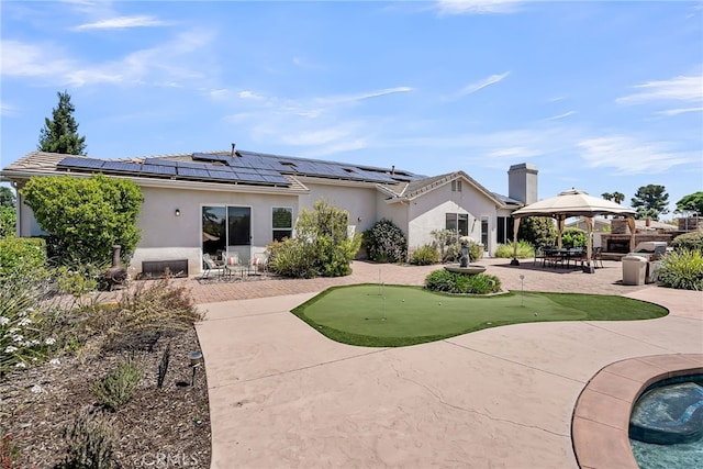 back of property with a putting green, a gazebo, a patio, stucco siding, and roof mounted solar panels