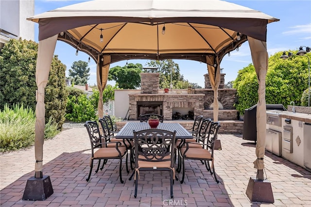 view of patio / terrace with a gazebo, an outdoor stone fireplace, outdoor dining space, exterior kitchen, and a sink