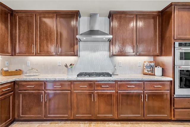 kitchen with wall chimney exhaust hood, stainless steel appliances, and light stone countertops