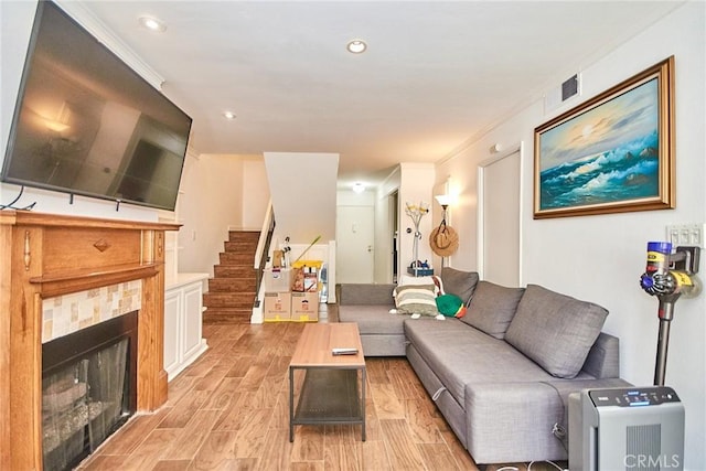 living area featuring stairs, light wood-style flooring, a tile fireplace, recessed lighting, and crown molding