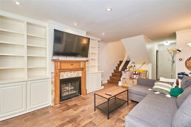 living area with stairway, a tiled fireplace, light wood-type flooring, ornamental molding, and recessed lighting