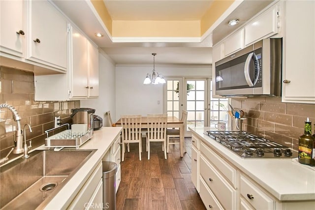 kitchen featuring stainless steel appliances, a sink, dark wood-type flooring, a tray ceiling, and white cabinetry