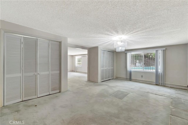 unfurnished living room with plenty of natural light, a chandelier, a textured ceiling, and carpet flooring