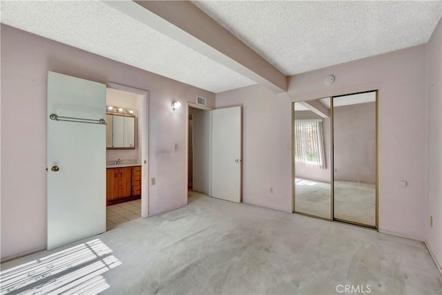 unfurnished bedroom featuring a textured ceiling, light colored carpet, connected bathroom, and a closet