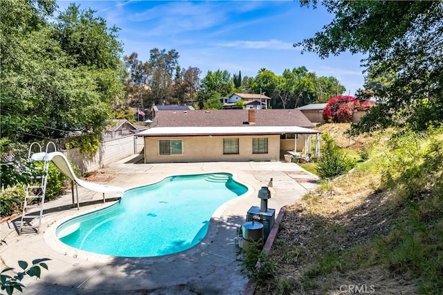 back of property featuring a patio, a fenced backyard, an outdoor pool, and view of wooded area