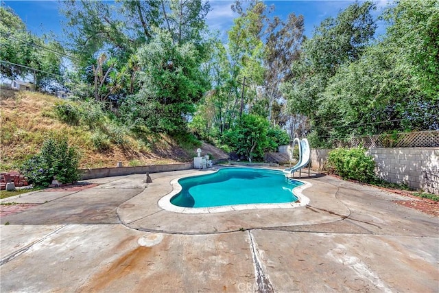 view of pool with a water slide, a patio, and view of scattered trees