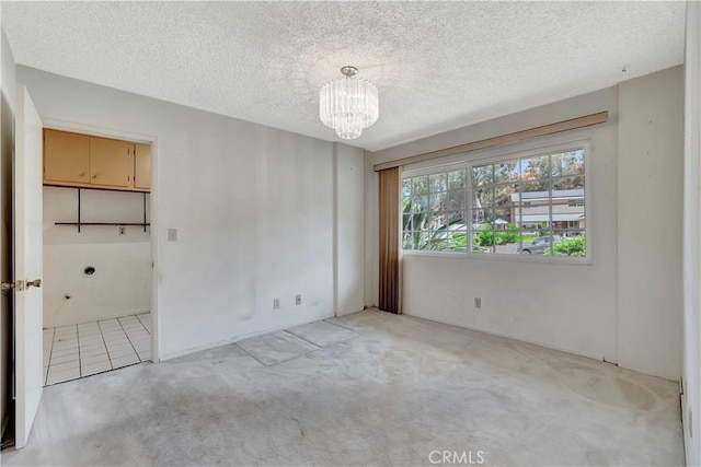 spare room featuring a chandelier, light carpet, and a textured ceiling