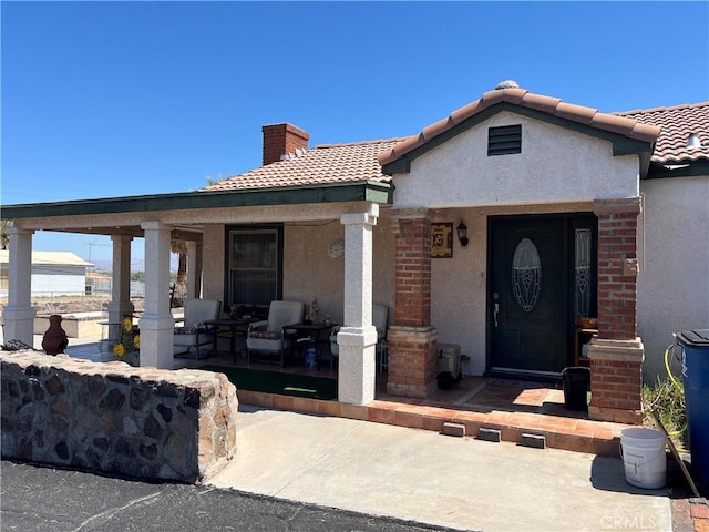 525 S L St, Needles, CA 92363 - view of exterior entry with covered porch, stucco siding, a chimney, and a tiled roof