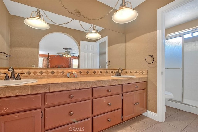 full bath with tile patterned flooring, a ceiling fan, a shower with shower door, double vanity, and a textured wall