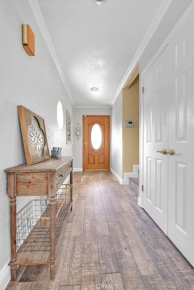 foyer featuring a textured ceiling, wood finished floors, ornamental molding, baseboards, and stairway