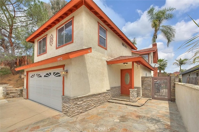 view of front facade featuring stucco siding, an attached garage, stone siding, a gate, and concrete driveway