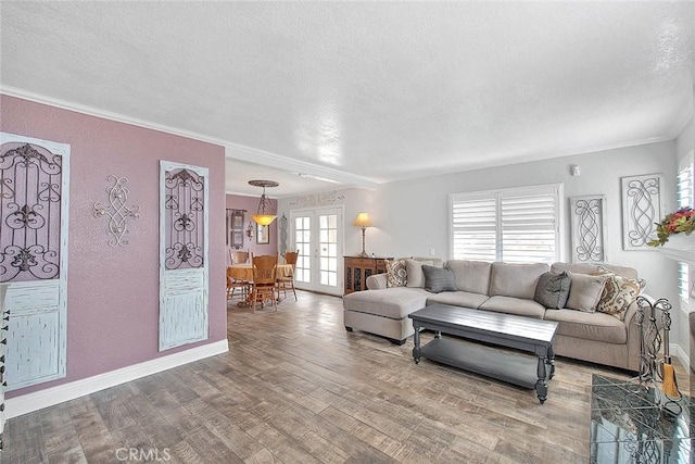 living area with french doors, a textured ceiling, wood finished floors, ornamental molding, and a textured wall
