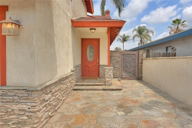 doorway to property with stucco siding, stone siding, and a gate