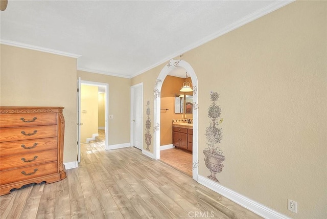unfurnished bedroom featuring arched walkways, light wood finished floors, connected bathroom, crown molding, and baseboards