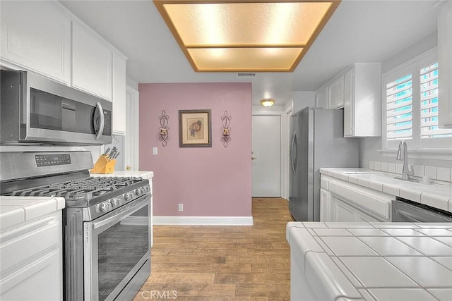 kitchen with appliances with stainless steel finishes, tile countertops, a sink, and white cabinetry