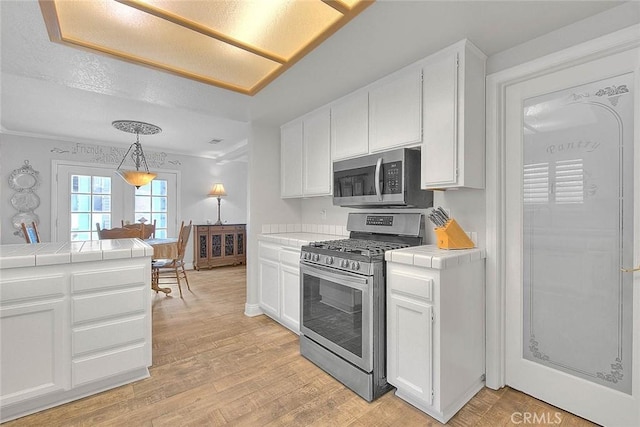 kitchen with appliances with stainless steel finishes, tile countertops, white cabinets, and light wood-type flooring