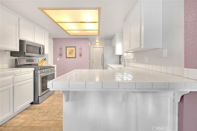 kitchen with appliances with stainless steel finishes, tile countertops, white cabinetry, and a peninsula