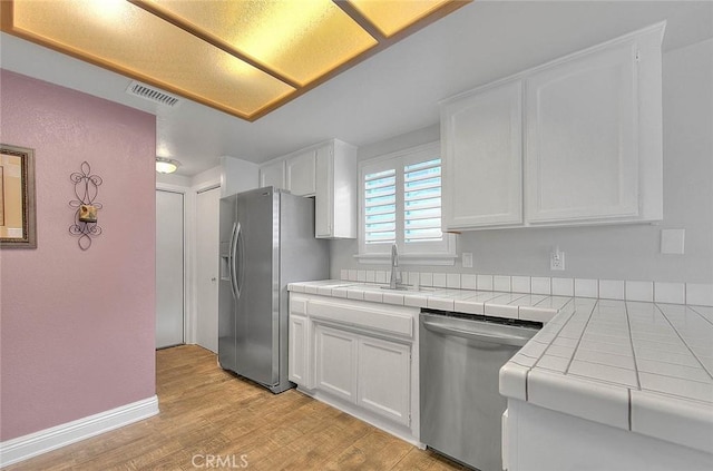 kitchen with stainless steel appliances, tile countertops, a sink, white cabinetry, and light wood-style flooring