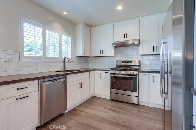 7411 Brava St, Carlsbad, CA 92009 - kitchen with appliances with stainless steel finishes, a sink, under cabinet range hood, dark countertops, and light wood-type flooring