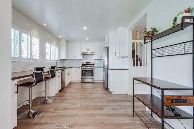 7411 Brava St, Carlsbad, CA 92009 - kitchen with stainless steel appliances, under cabinet range hood, white cabinetry, dark countertops, and recessed lighting
