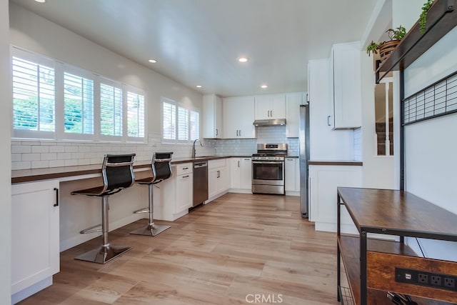7411 Brava St, Carlsbad, CA 92009 - kitchen featuring stainless steel appliances, under cabinet range hood, light wood-style floors, dark countertops, and a sink