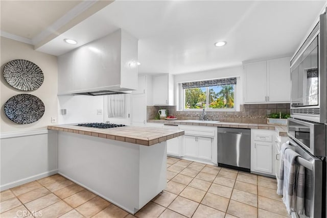 25001 Mackenzie St, Laguna Hills, CA 92653 - kitchen featuring appliances with stainless steel finishes, tile counters, a peninsula, tasteful backsplash, and white cabinetry