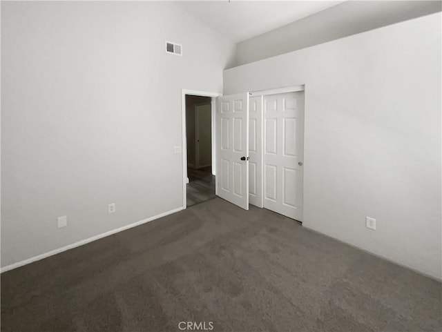 unfurnished bedroom featuring carpet flooring, high vaulted ceiling, a closet, and baseboards