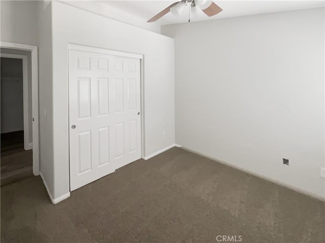 unfurnished bedroom featuring dark colored carpet, baseboards, a closet, and a ceiling fan