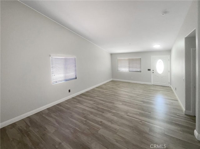 unfurnished living room with wood finished floors, vaulted ceiling, and baseboards