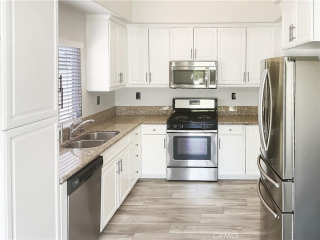 kitchen with stainless steel appliances, a sink, white cabinetry, stone counters, and light wood-style floors