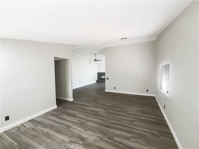 spare room featuring a ceiling fan, dark wood-type flooring, baseboards, and a fireplace
