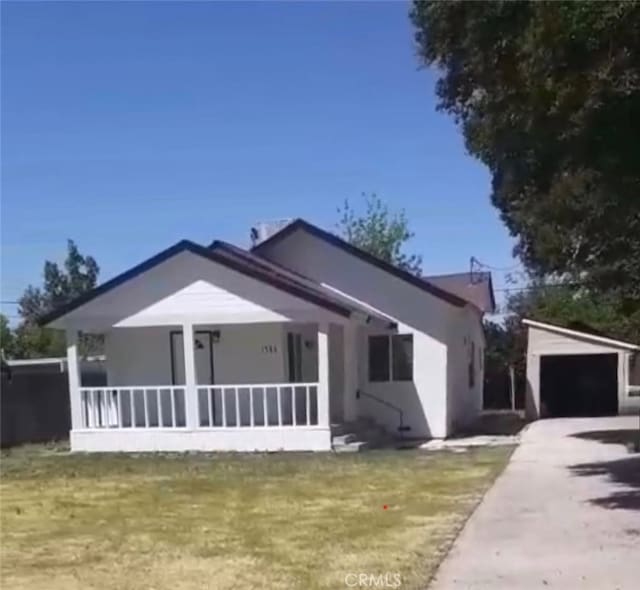 view of front of house featuring concrete driveway, an outbuilding, a front lawn, covered porch, and a detached garage