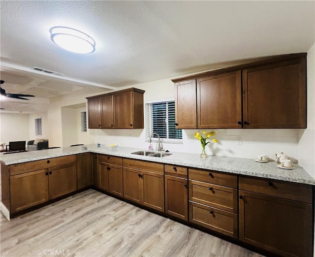 1385 N San Pablo Ave, Fresno, CA 93728 - kitchen featuring a sink, light wood finished floors, a peninsula, light stone counters, and a textured ceiling