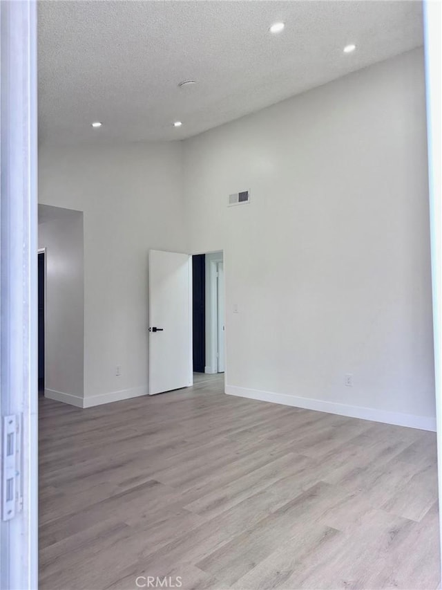 spare room featuring light wood-style floors, recessed lighting, a textured ceiling, a high ceiling, and baseboards