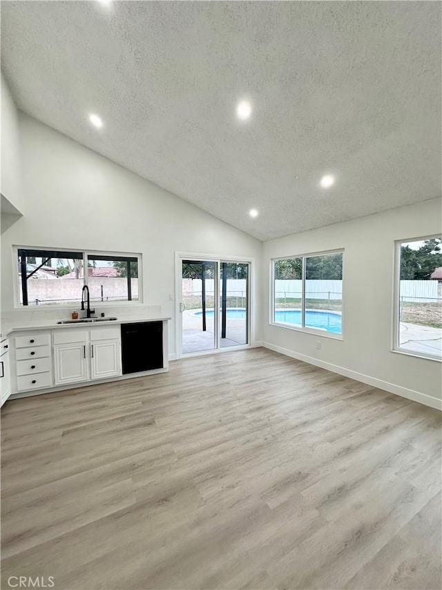 unfurnished living room with a sink, a textured ceiling, recessed lighting, light wood-style flooring, and baseboards
