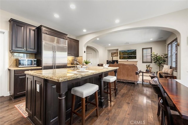 24 Tree Clover, Irvine, CA 92618 - kitchen featuring arched walkways, appliances with stainless steel finishes, a breakfast bar, decorative backsplash, and dark wood finished floors